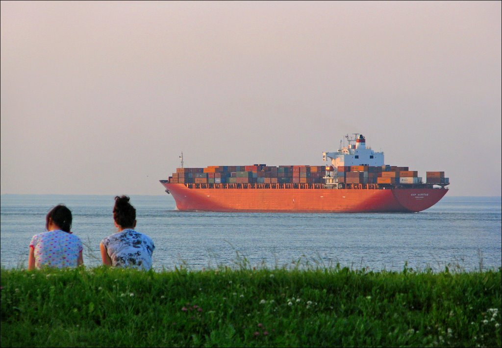 Fernweh? Zwei Mädchen sitzen abends auf dem Deich und schauen der "Cap Akritas" aus Hongkong hinterher