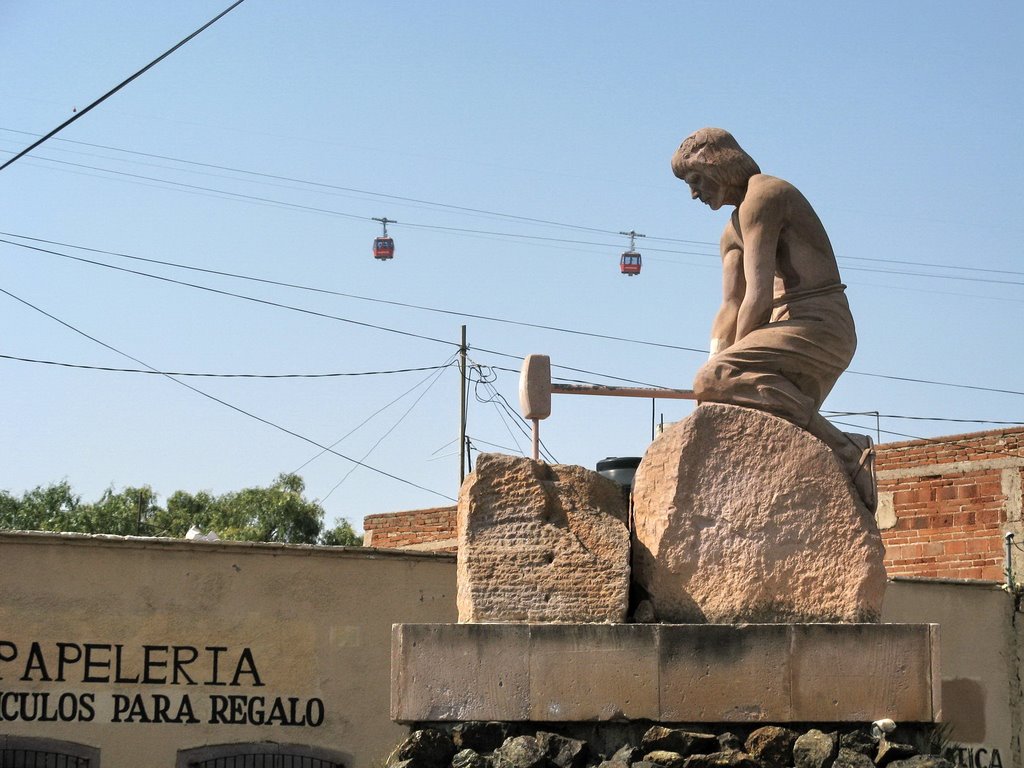 Two cablecars are crossing behind a statue of a worker with a hammer