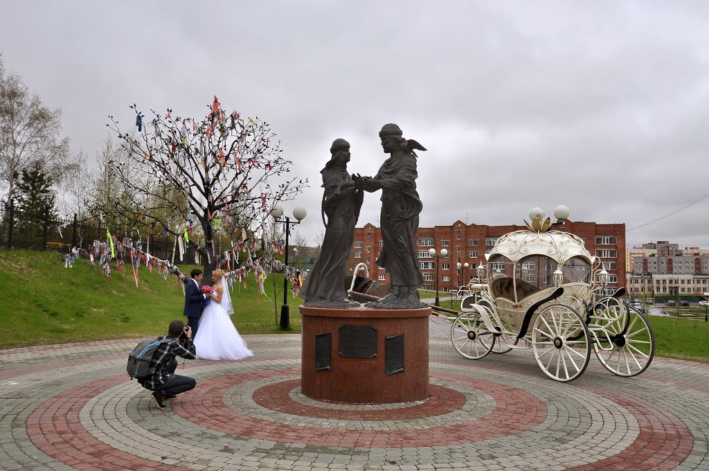 Newlyweds at the tree of fulfillment of a wishes near monument to Saints Peter and Fevronia of Murom