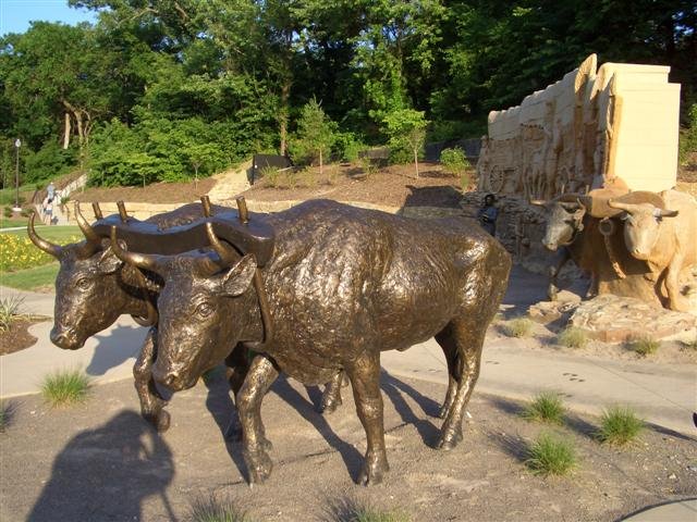 wagon train, life-size, clay/stone facade, clay/stone/bronze oxen, bronze oxen, and bronze woman with child, Pioneer Crossing Park,Shawnee,KS
